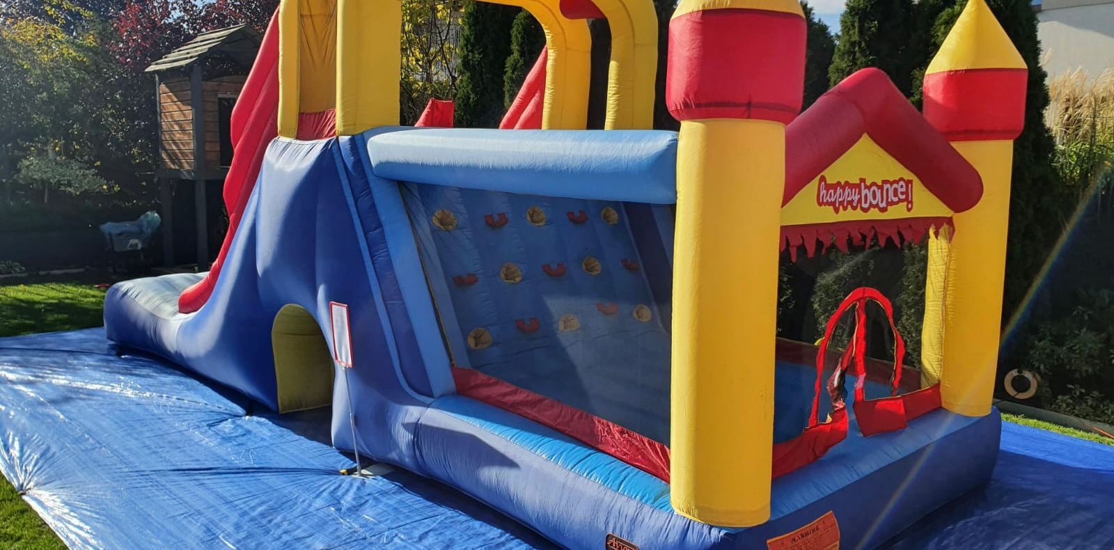 Hüpfburg – aufblasbare Burg mit Rutsche und Kletterwand auf einer Plane im Garten